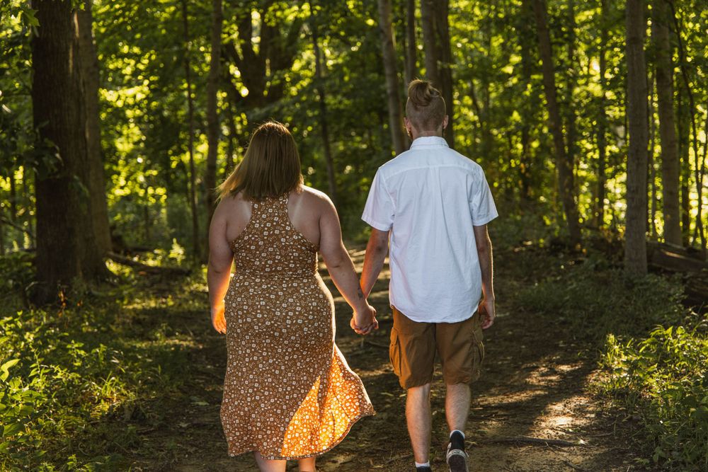 A couple walks hand in hand down a forest path during sunset.