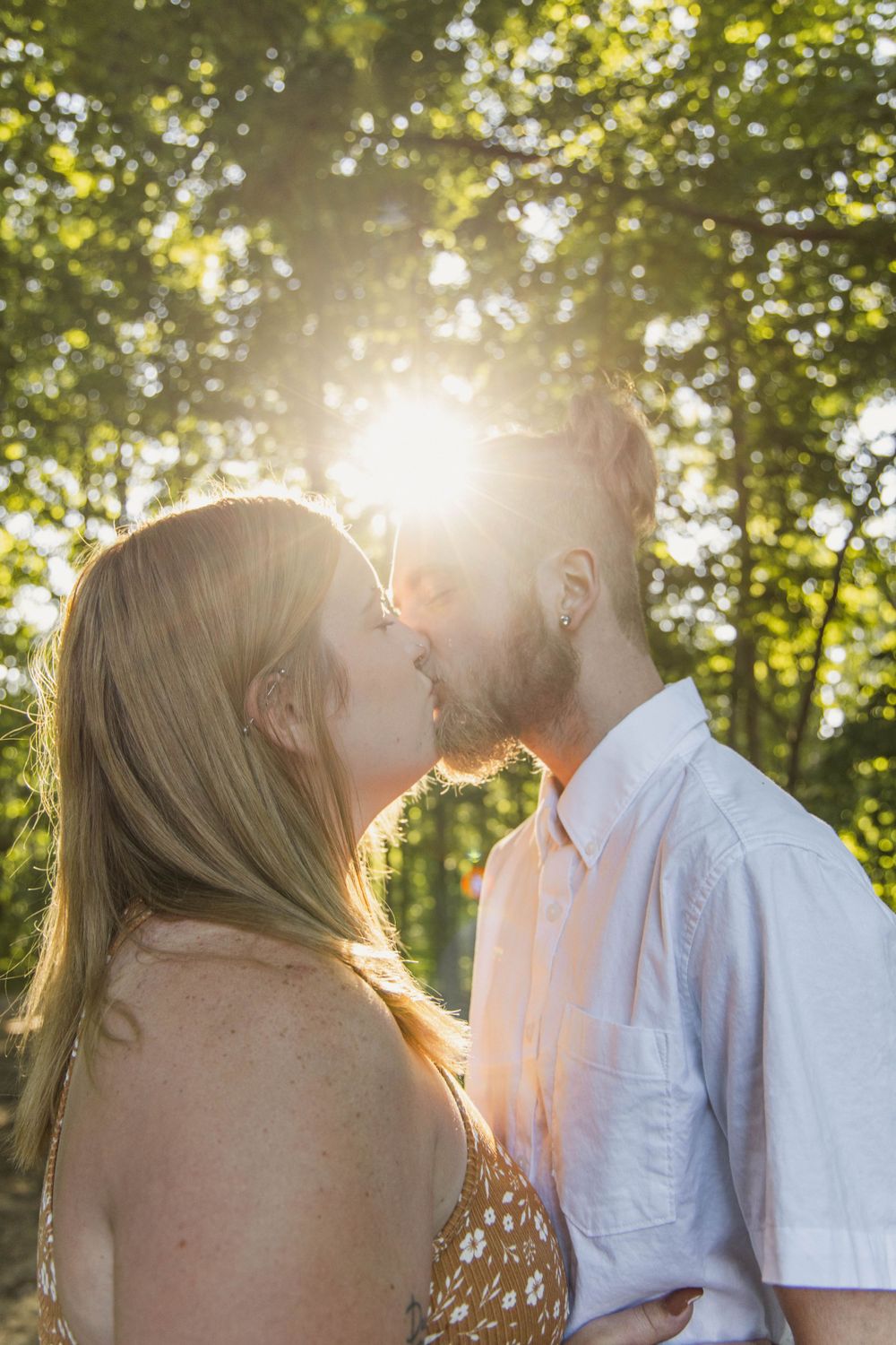 An intimate couple's portrait backlit by sunlight filtering through green trees.