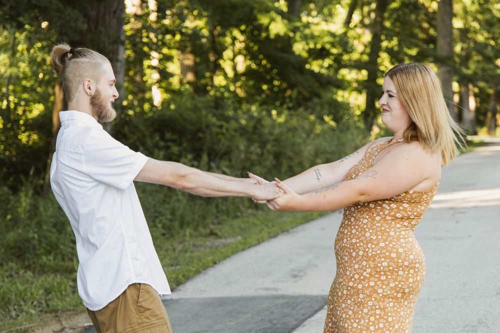 A playful couple holding hands and dancing on a path surrounded by greenery.