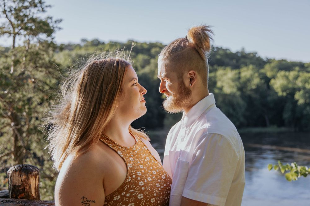 A couple poses for a romantic portrait by a river on a sunny day.