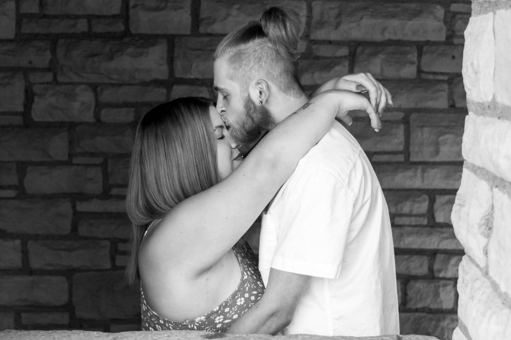 A romantic couple embraces against a brick wall backdrop in black and white.