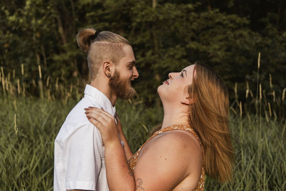 A couple shares an intimate moment while laughing together in a summer field.