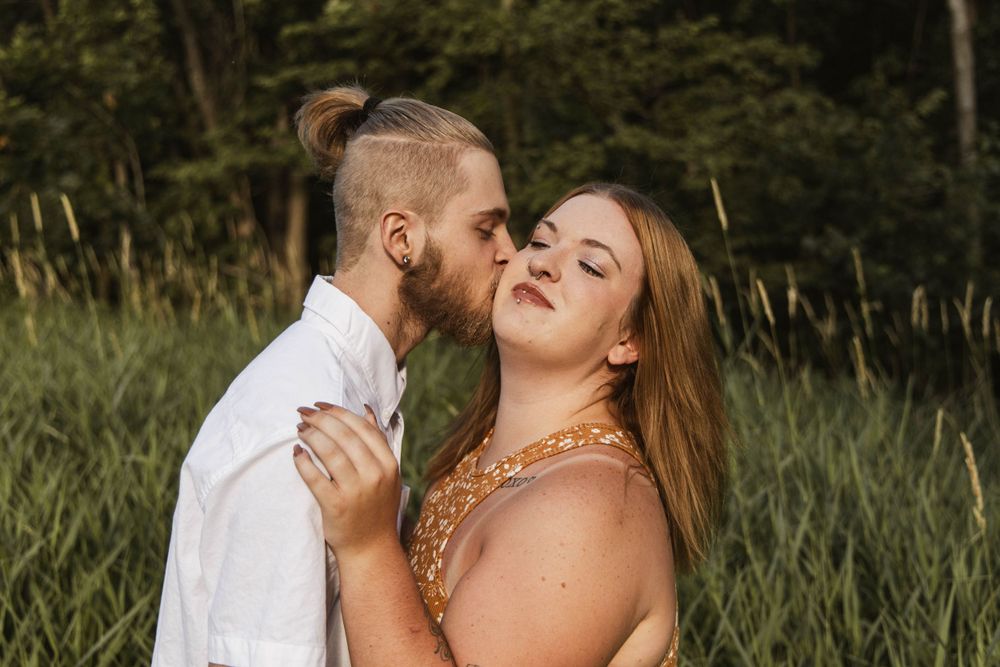 A tender moment between a couple captured in warm sunlight with natural foliage background.