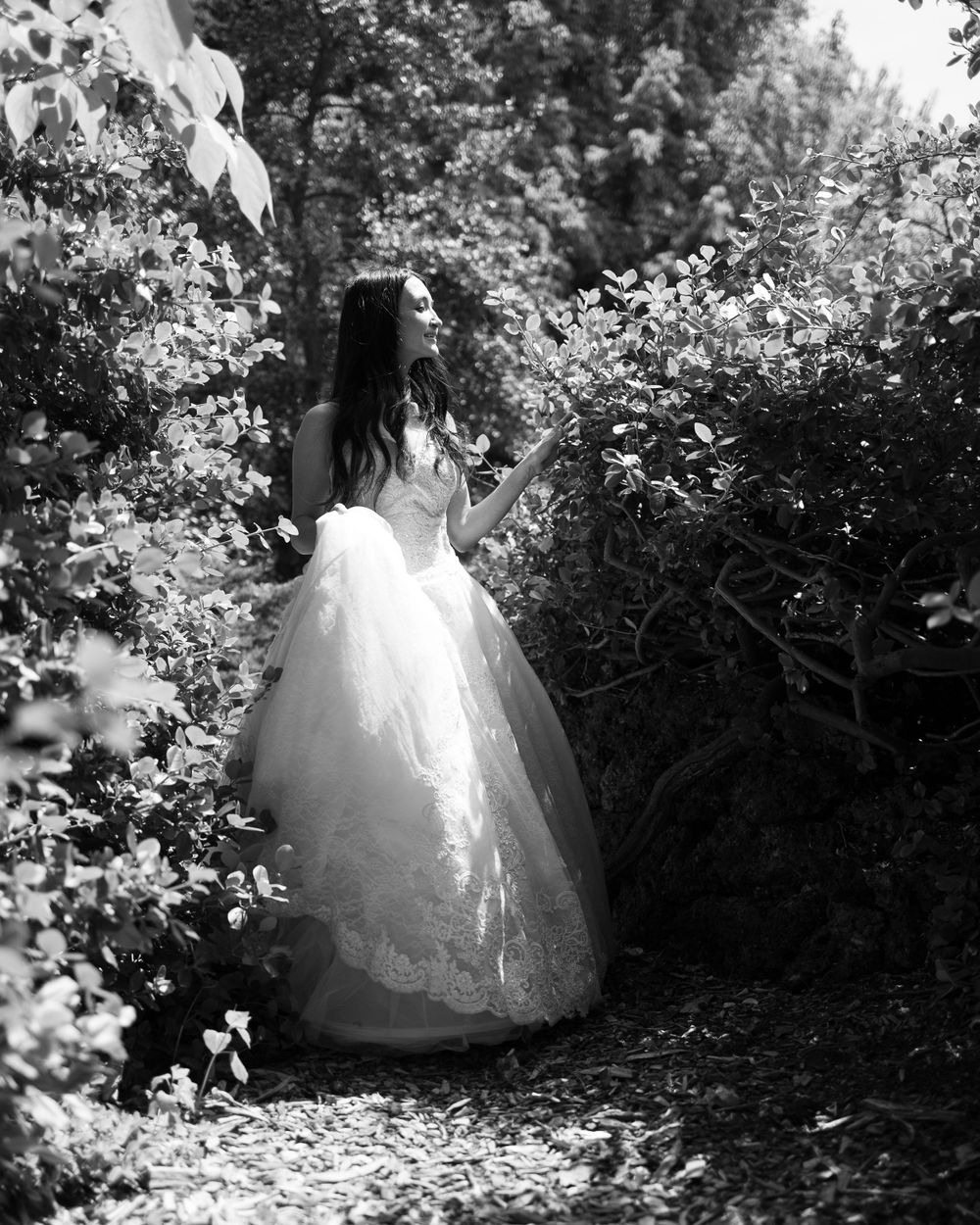 A dreamy black and white portrait of a person in a wedding gown among blooming garden flowers.
