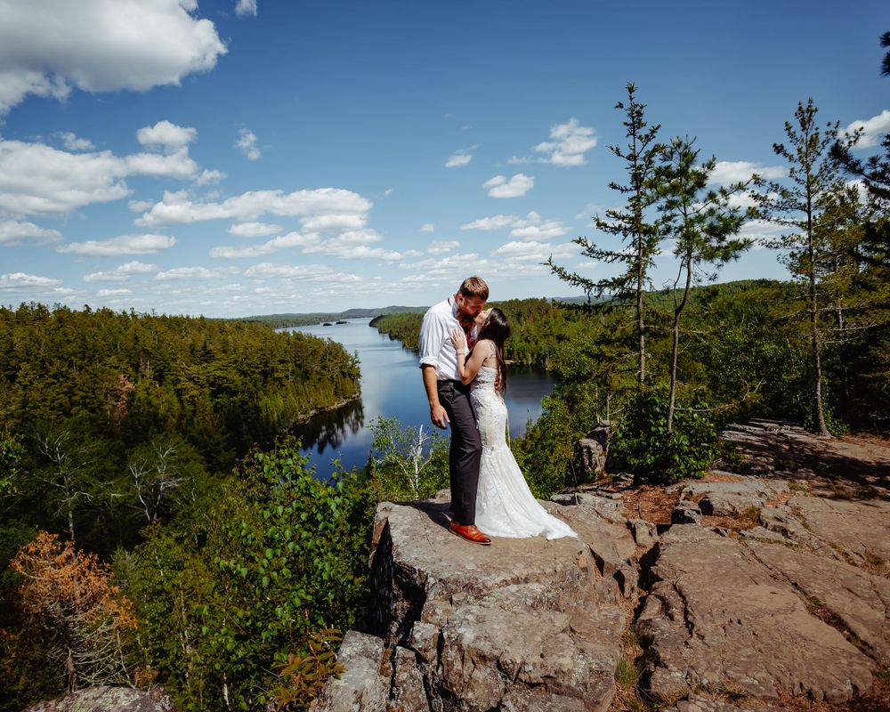 Romantic wedding moment captured on cliff edge with stunning forest and river backdrop.