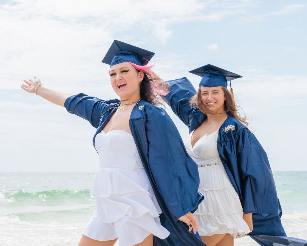 Two happy graduates in blue caps and gowns celebrating on a sunny beach together.