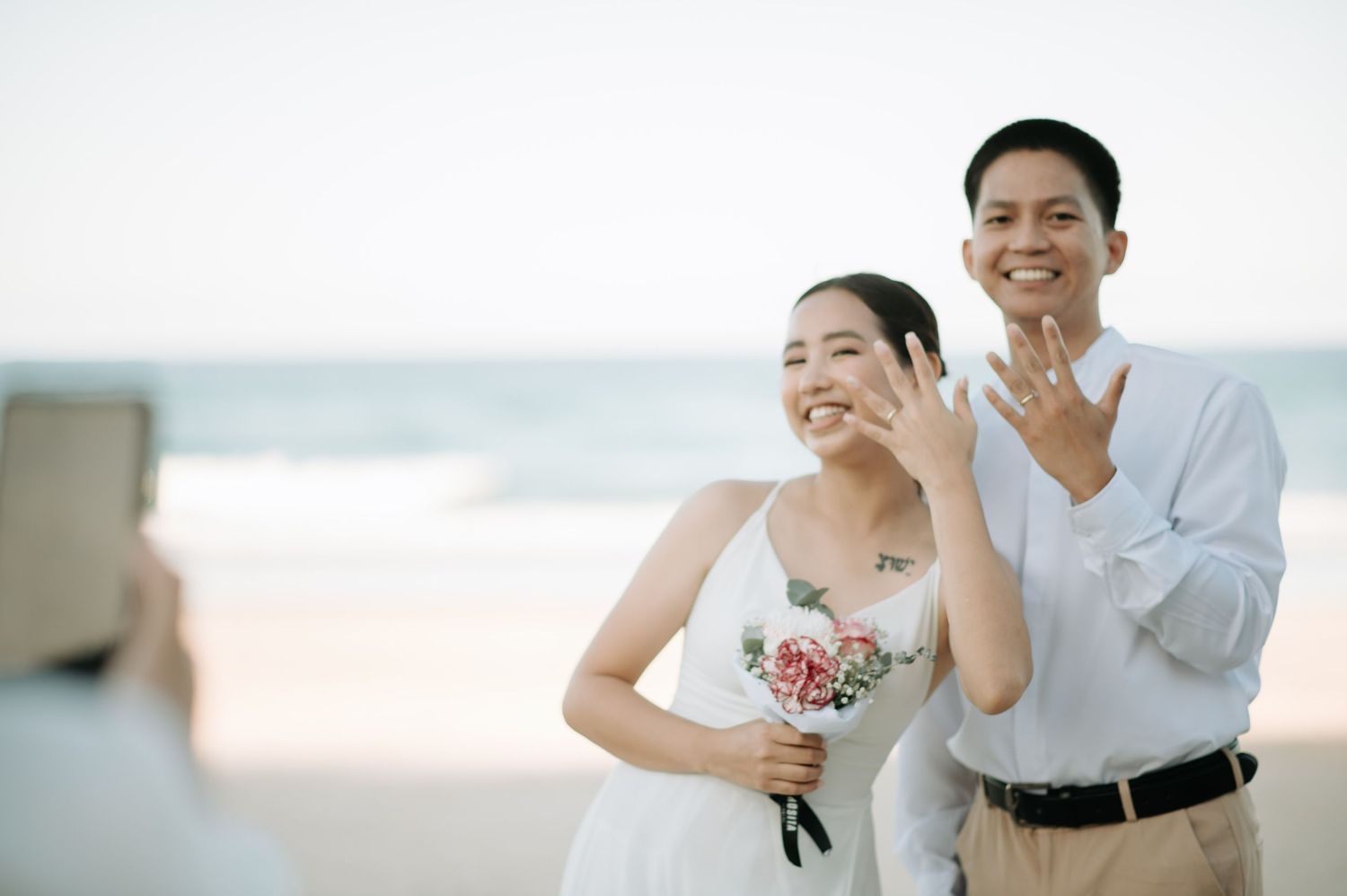 Couple in wedding attire laughing together on a sunny beach.
