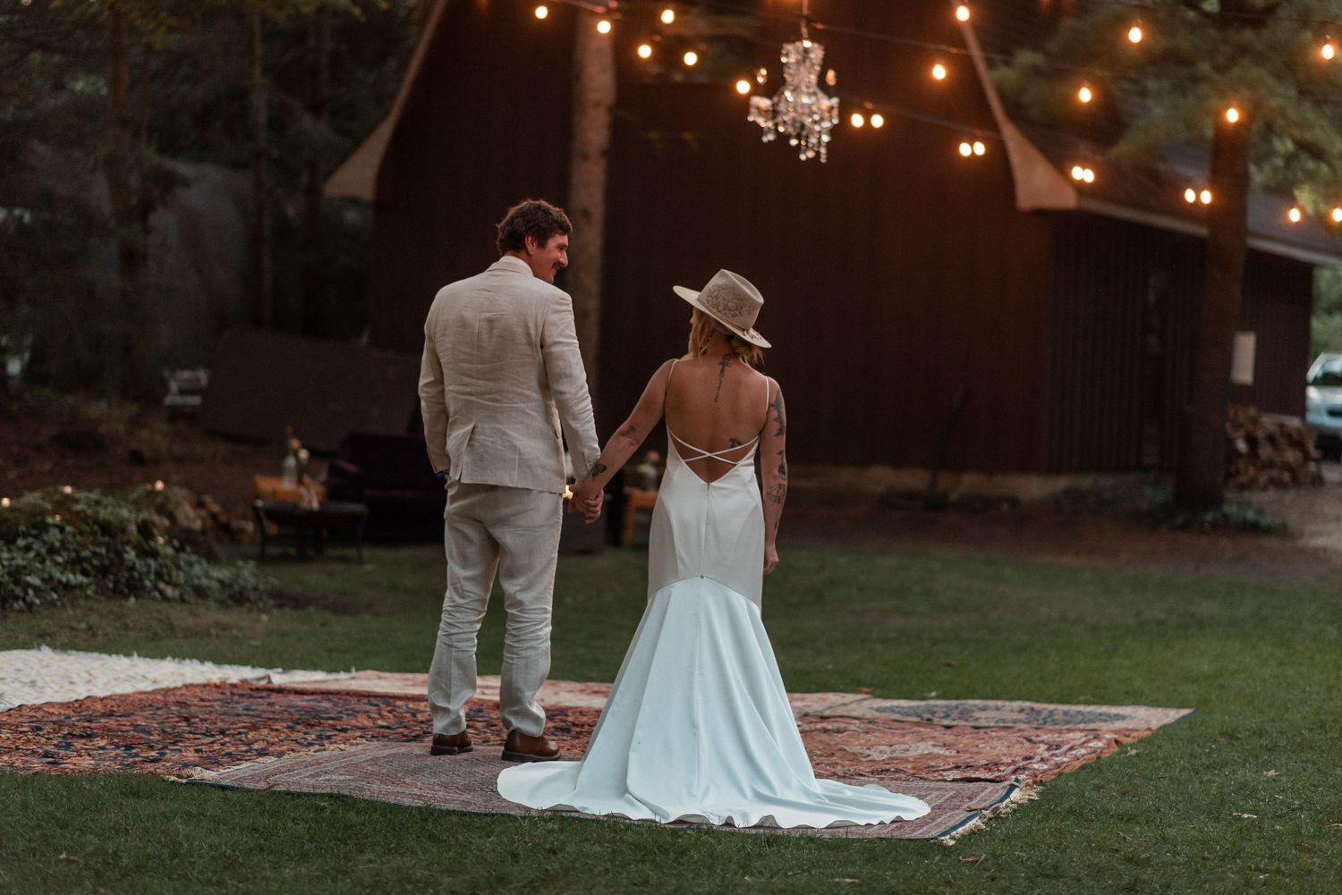 Romantic sunset wedding scene with couple standing on outdoor dance floor under string lights.