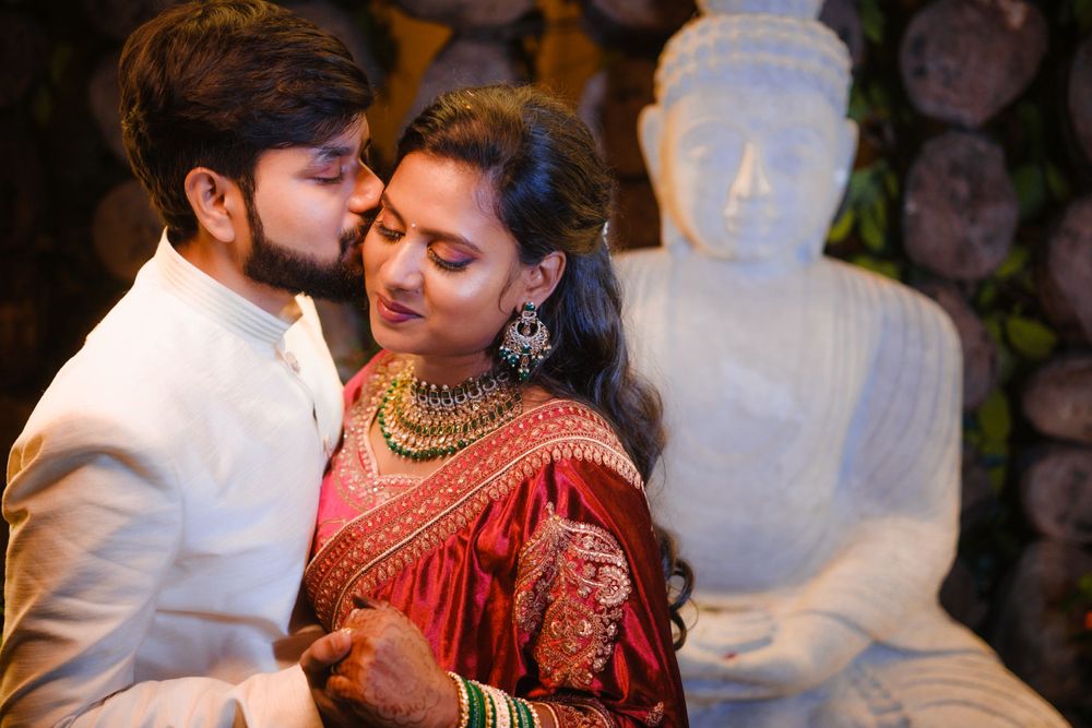 Intimate moment captured with traditional Indian attire against Buddha statue backdrop.