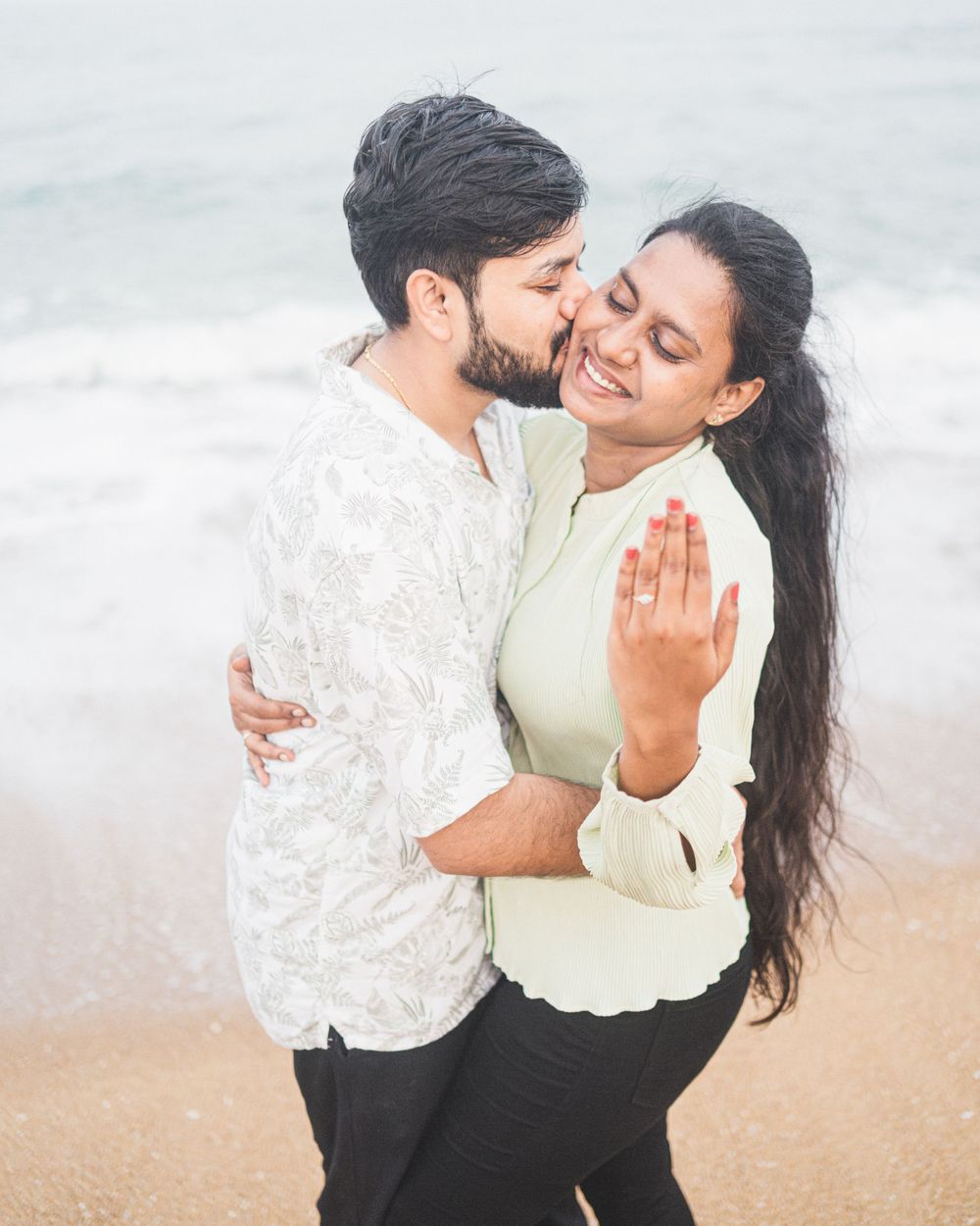 Romantic couple embracing on a misty beach with waves crashing in the background.