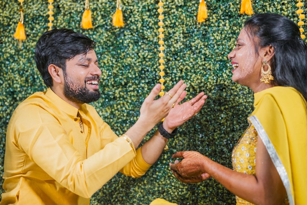 Wedding celebration with couple in yellow outfits against a green backdrop with hanging decorations.