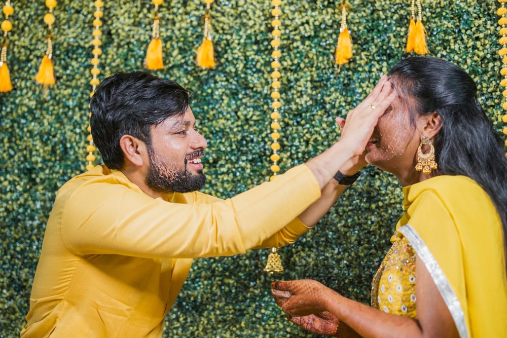 Traditional Haldi ceremony moment captured against green and yellow decorated backdrop.