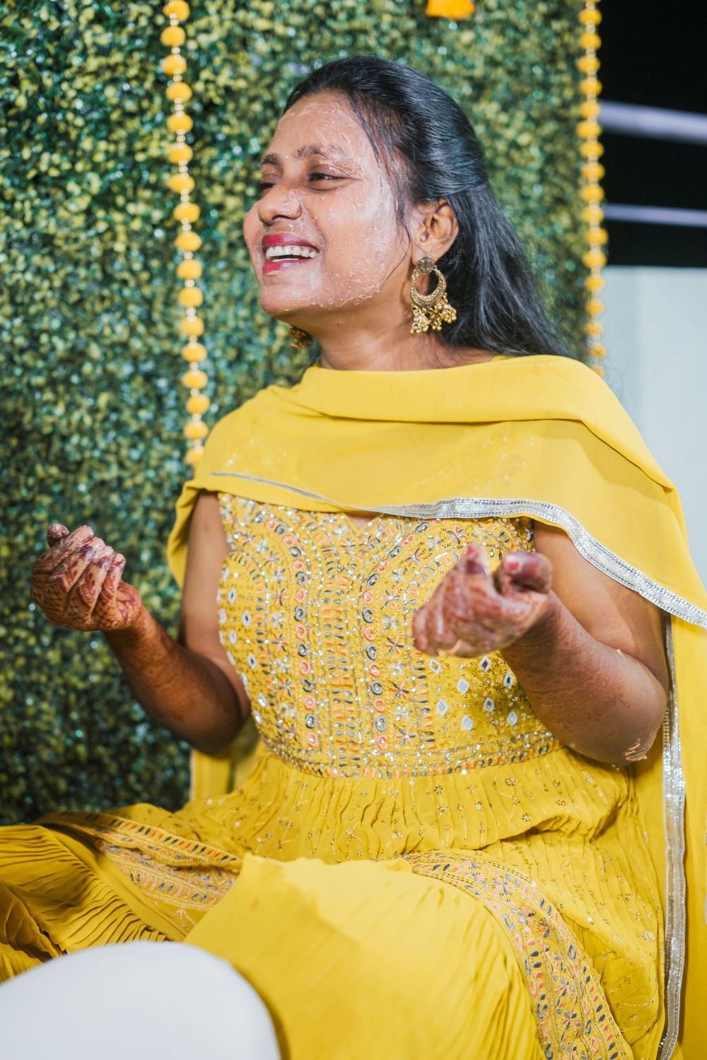 Woman in yellow traditional dress laughing joyfully during celebration with decorative backdrop.
