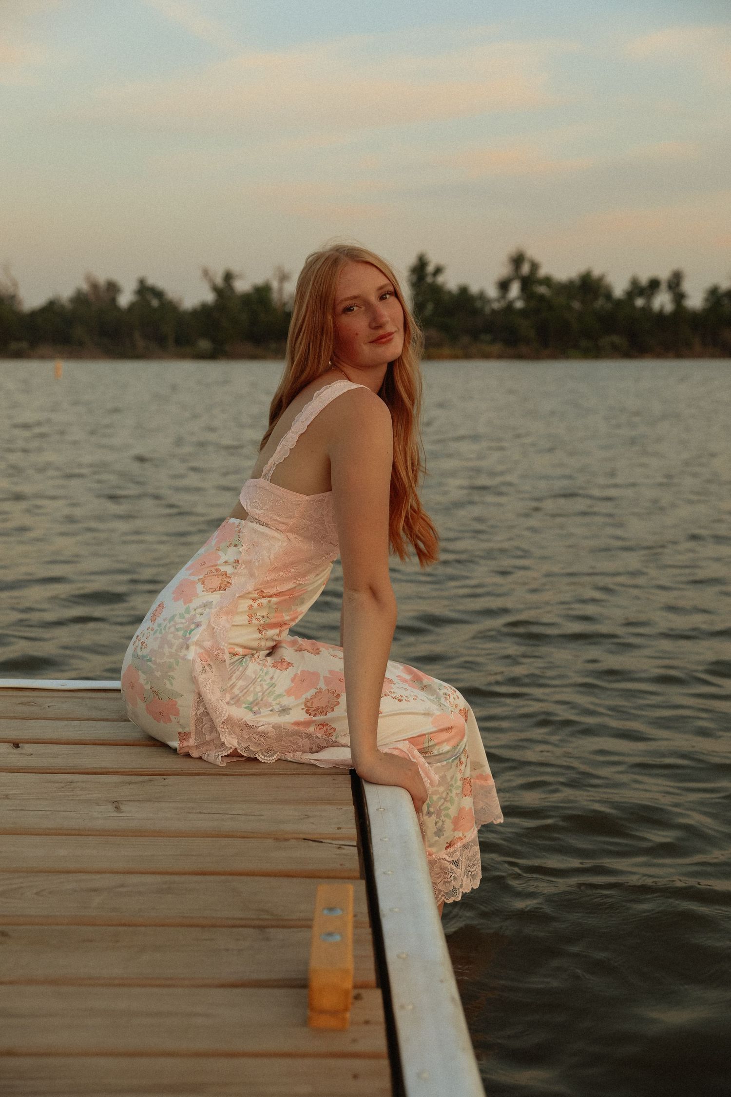 A dreamy sunset photoshoot on a wooden dock over calm waters with flowing dress and golden light.