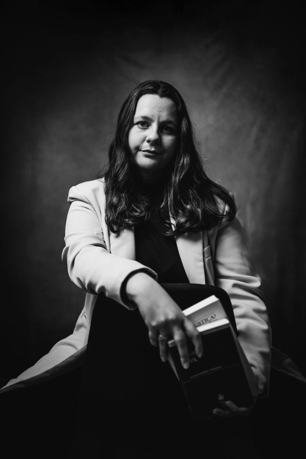 Black and white portrait of person in light blazer holding book with dramatic studio lighting.