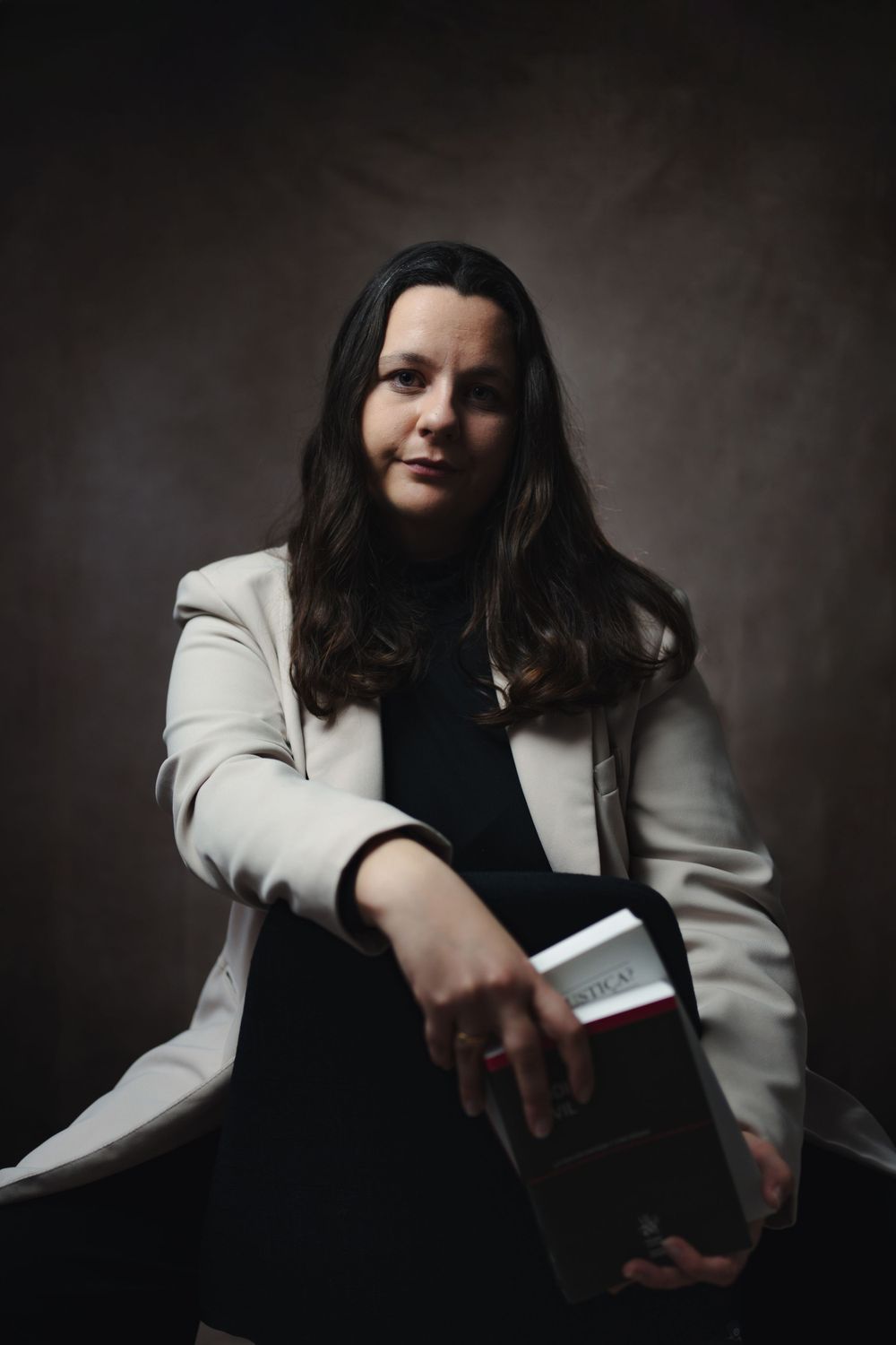 Artistic studio portrait of person in white blazer holding book with moody lighting.