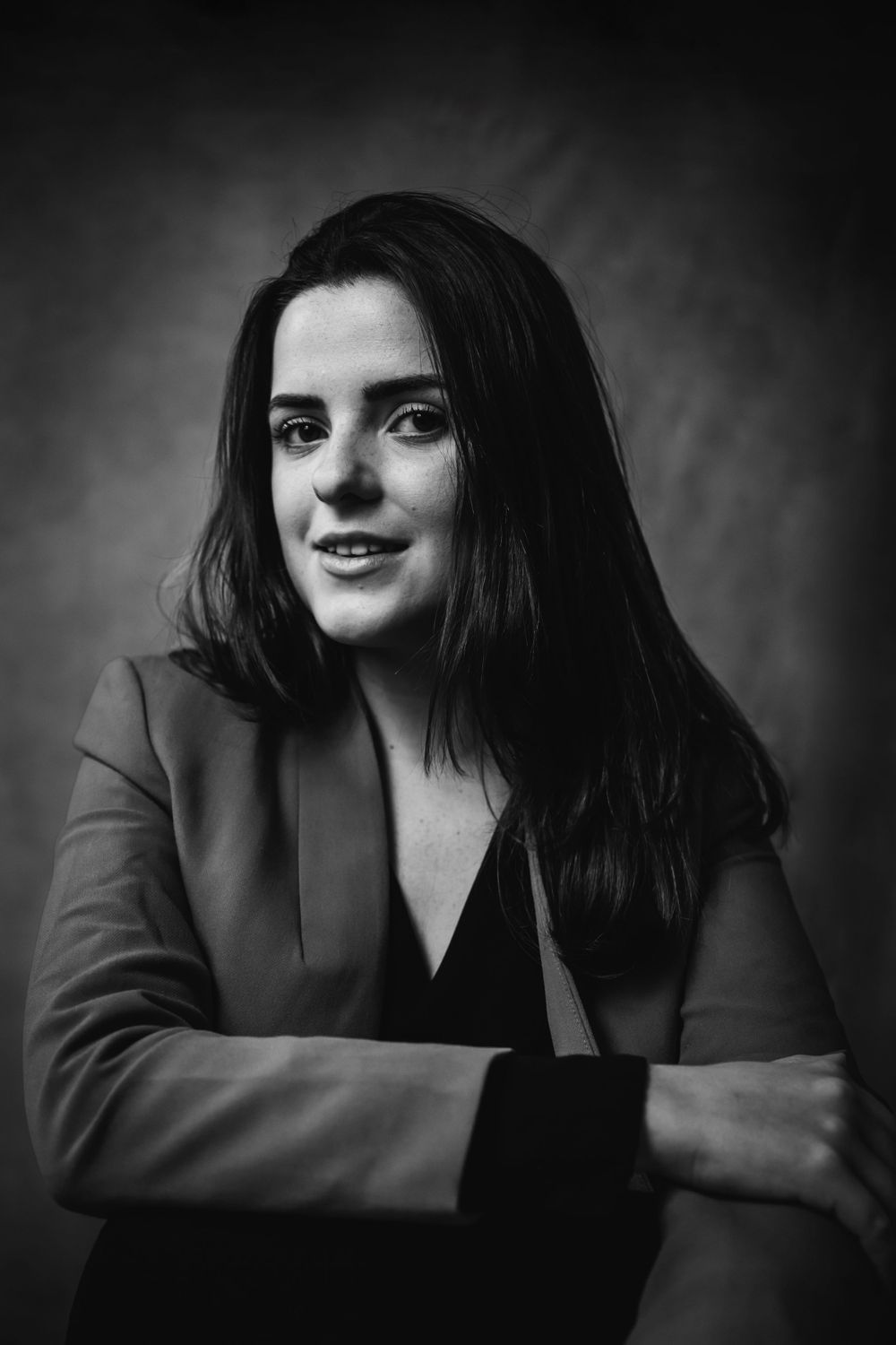 Monochrome professional headshot of person in blazer smiling against dark backdrop.