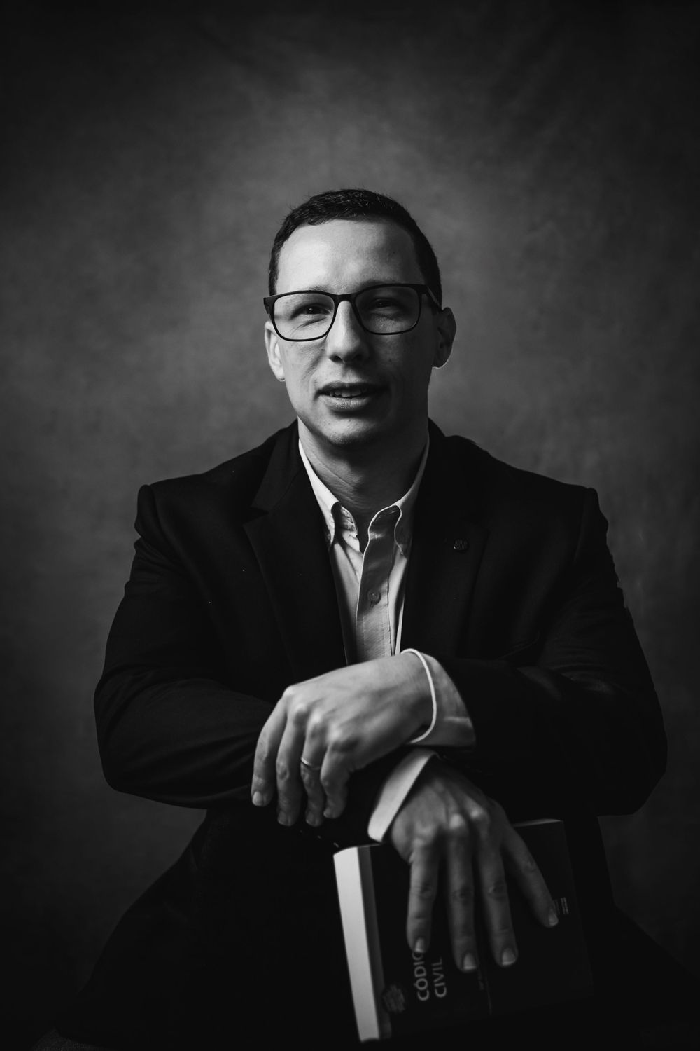 Monochrome headshot of professional in blazer and glasses holding book.