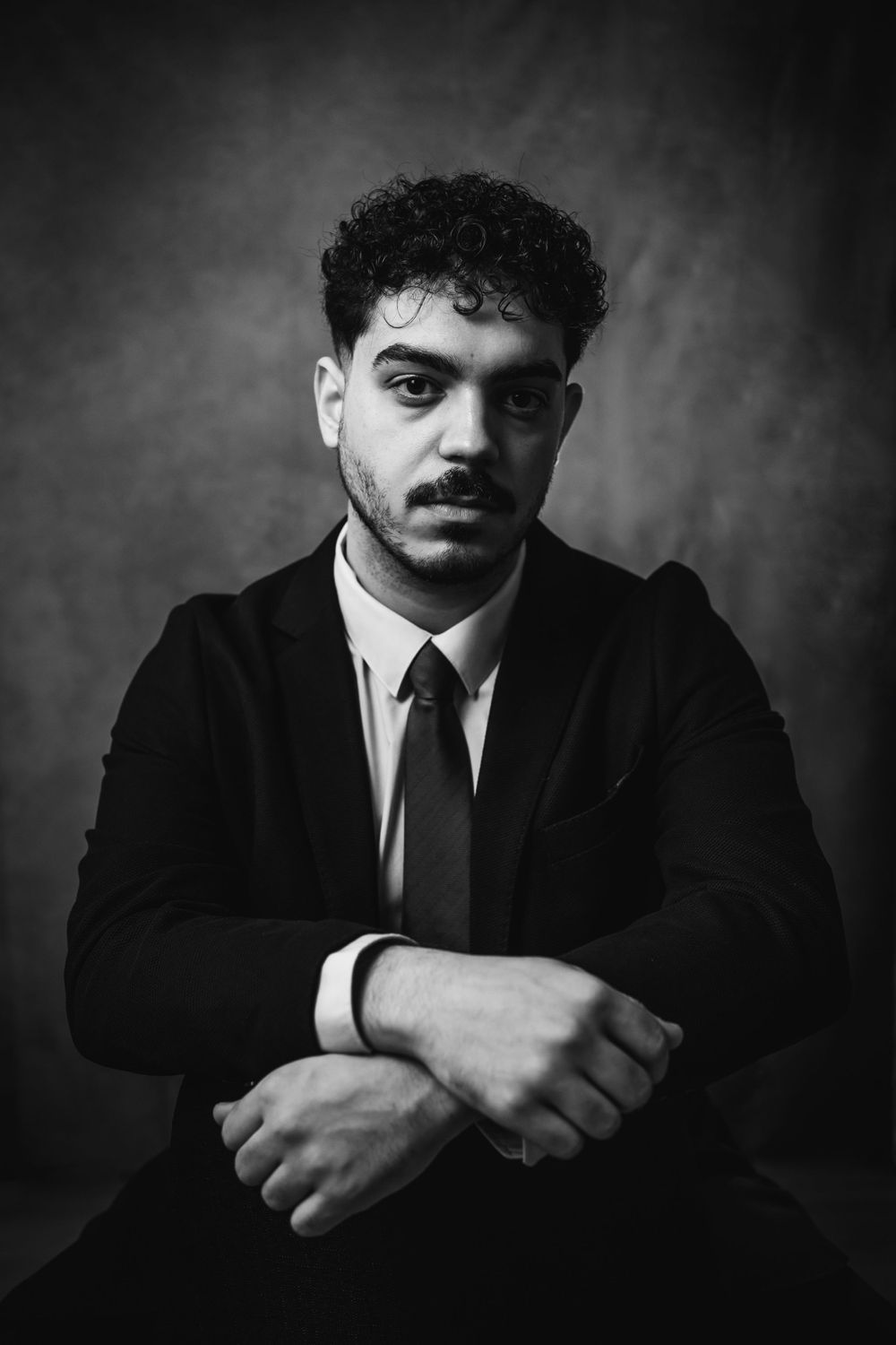 Dramatic black and white headshot of professional in suit and tie against dark background.