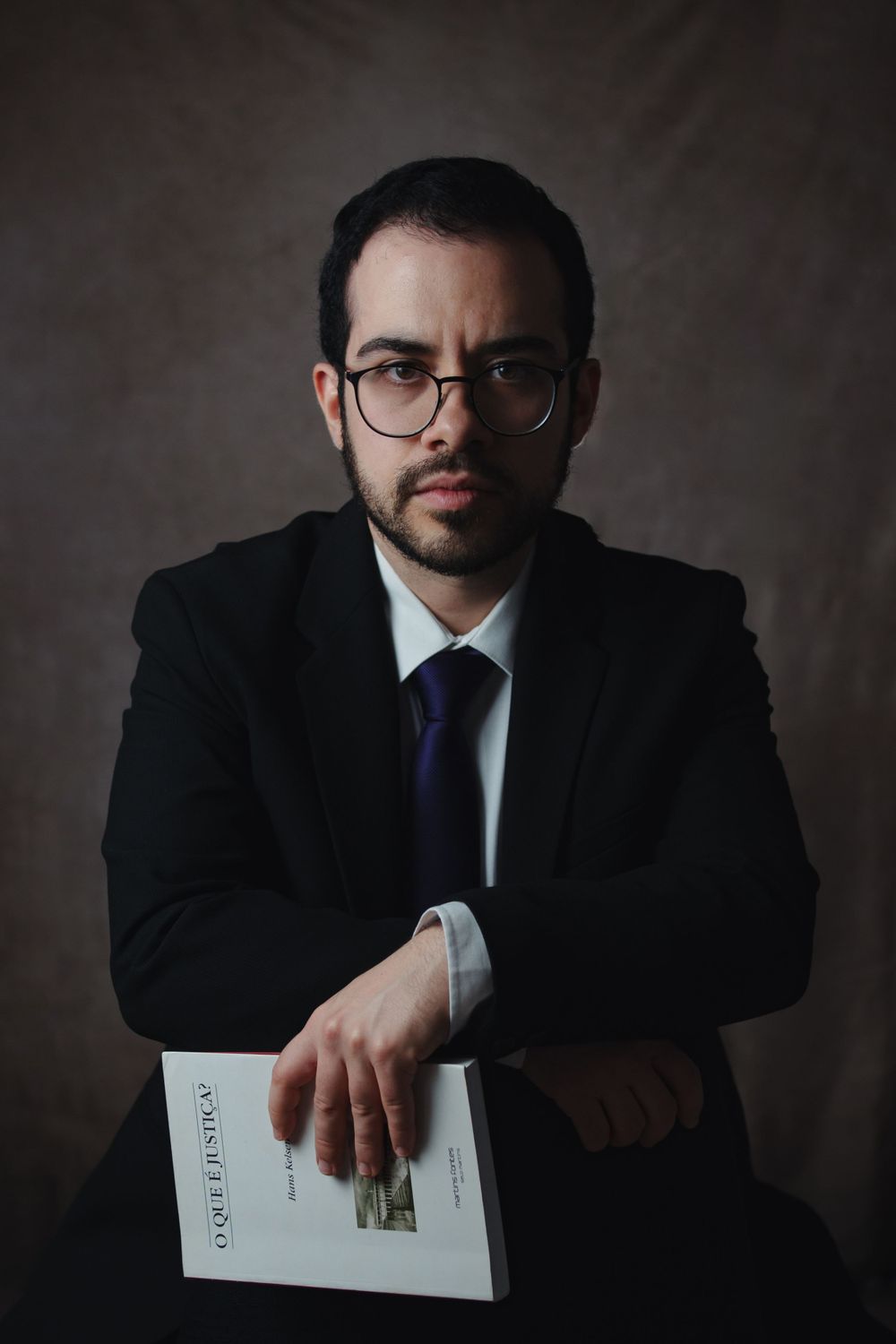 Business portrait of professional in suit and tie holding book against dark background.
