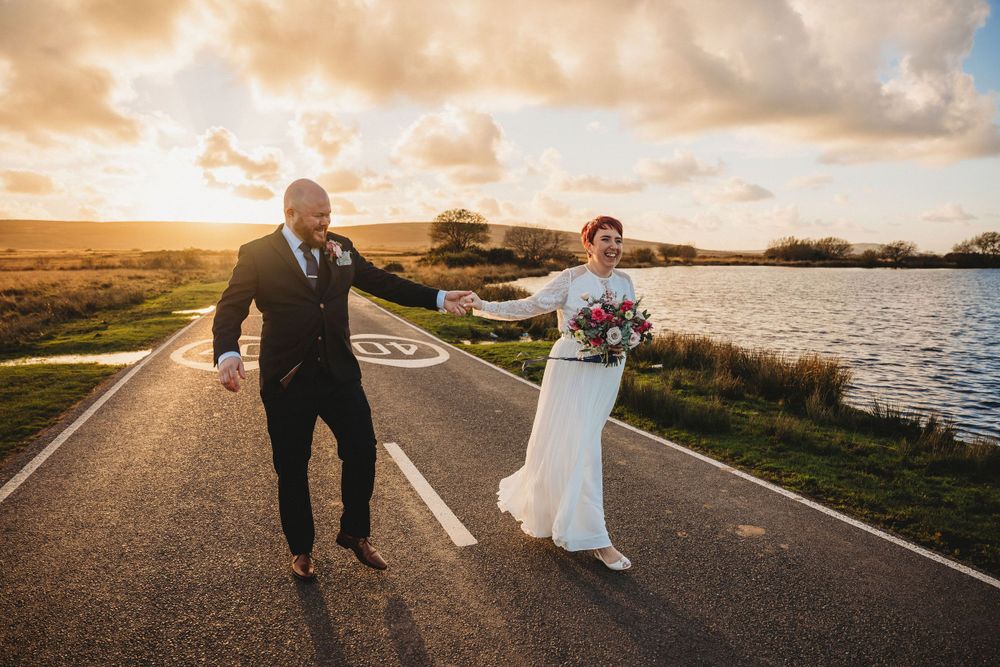 Joyful couple walking along a lakeside road during golden hour.