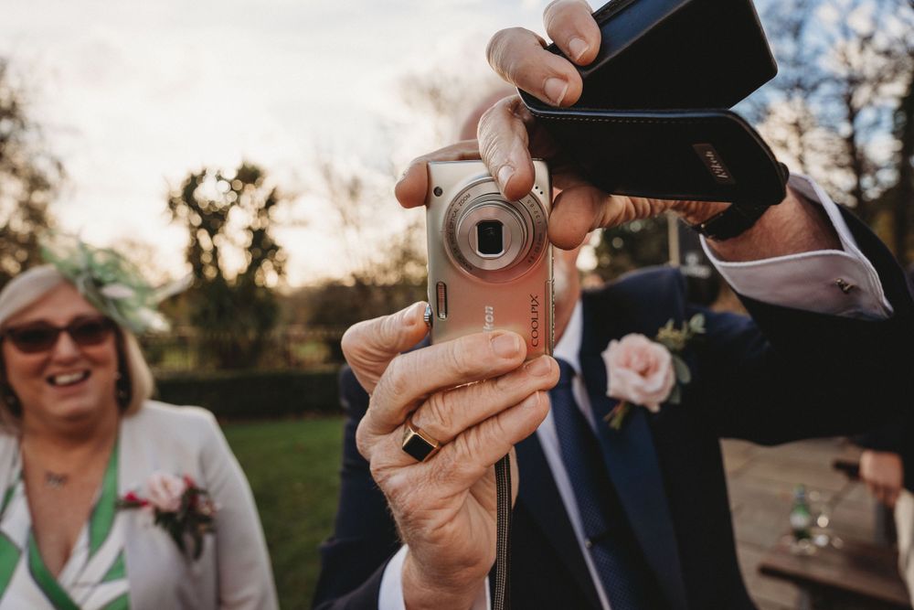 Close-up of hands holding a vintage camera during outdoor wedding celebrations.