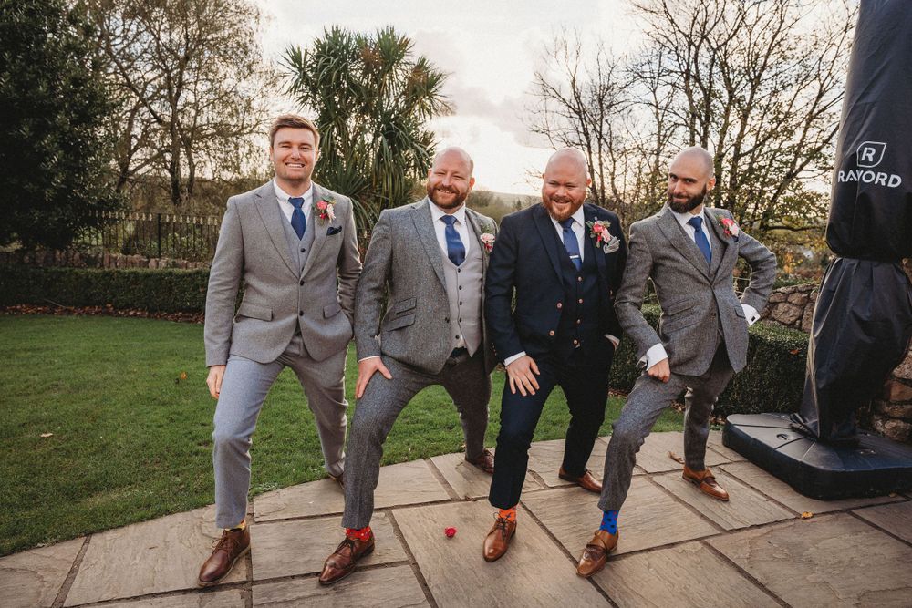 Groomsmen in grey suits showing off colorful socks while posing on stone steps.