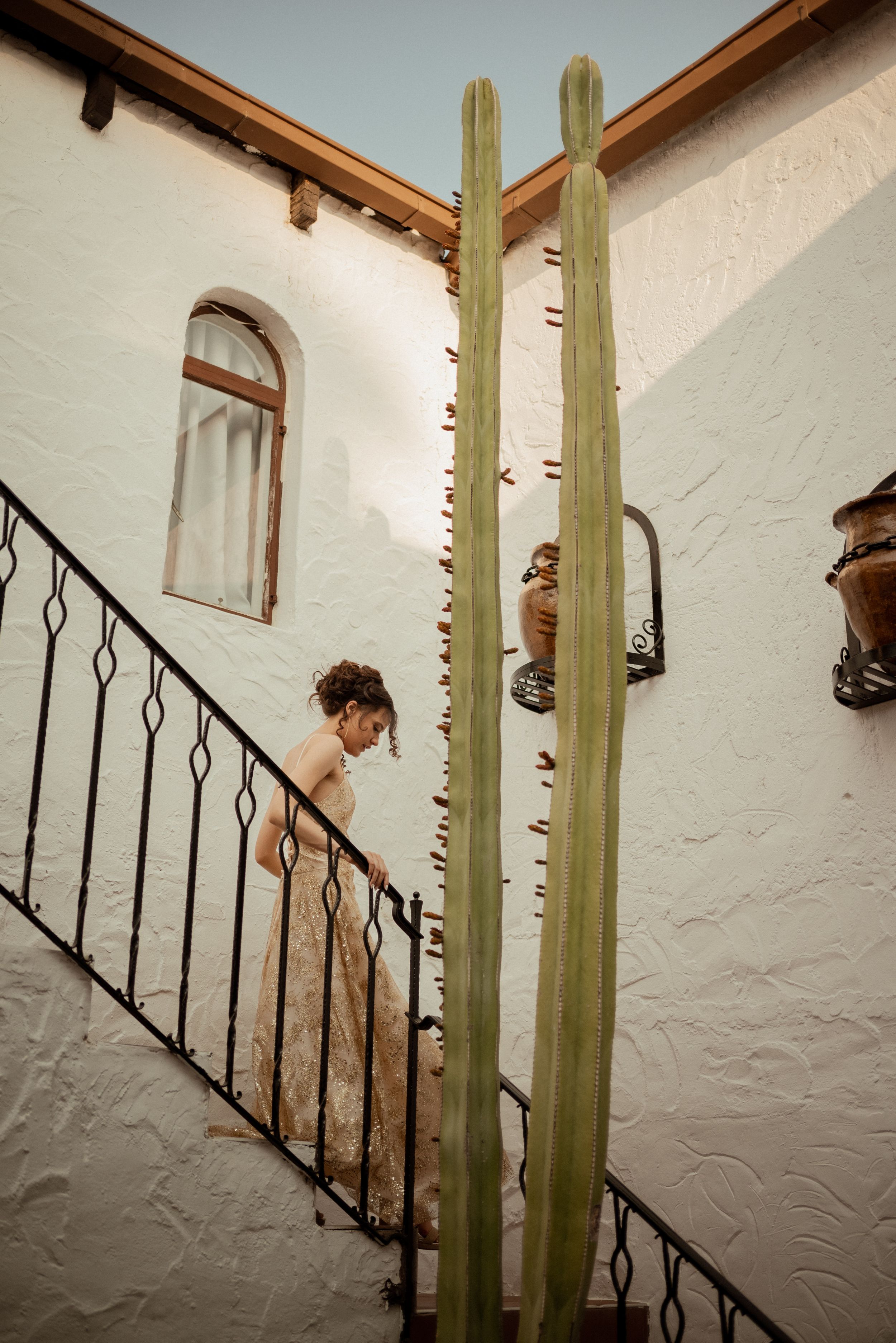 Person ascending staircase next to tall cactus plants against white Spanish-style wall.