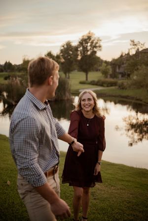 Couple shares joyful moment by scenic pond at sunset with trees in background.