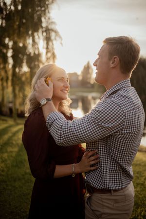 Romantic couple embraces outdoors during golden hour with autumn trees in background.