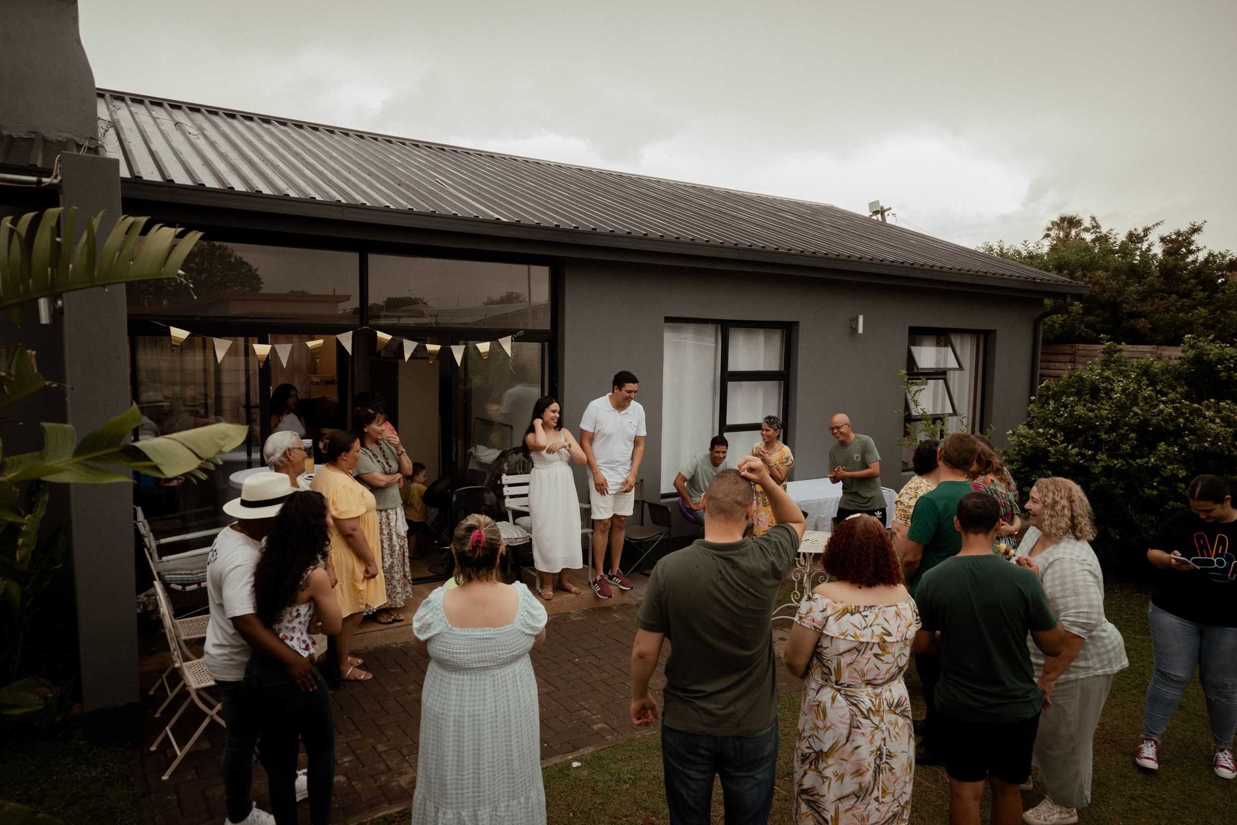 A small outdoor gathering of people watching a ceremony under string lights at dusk.