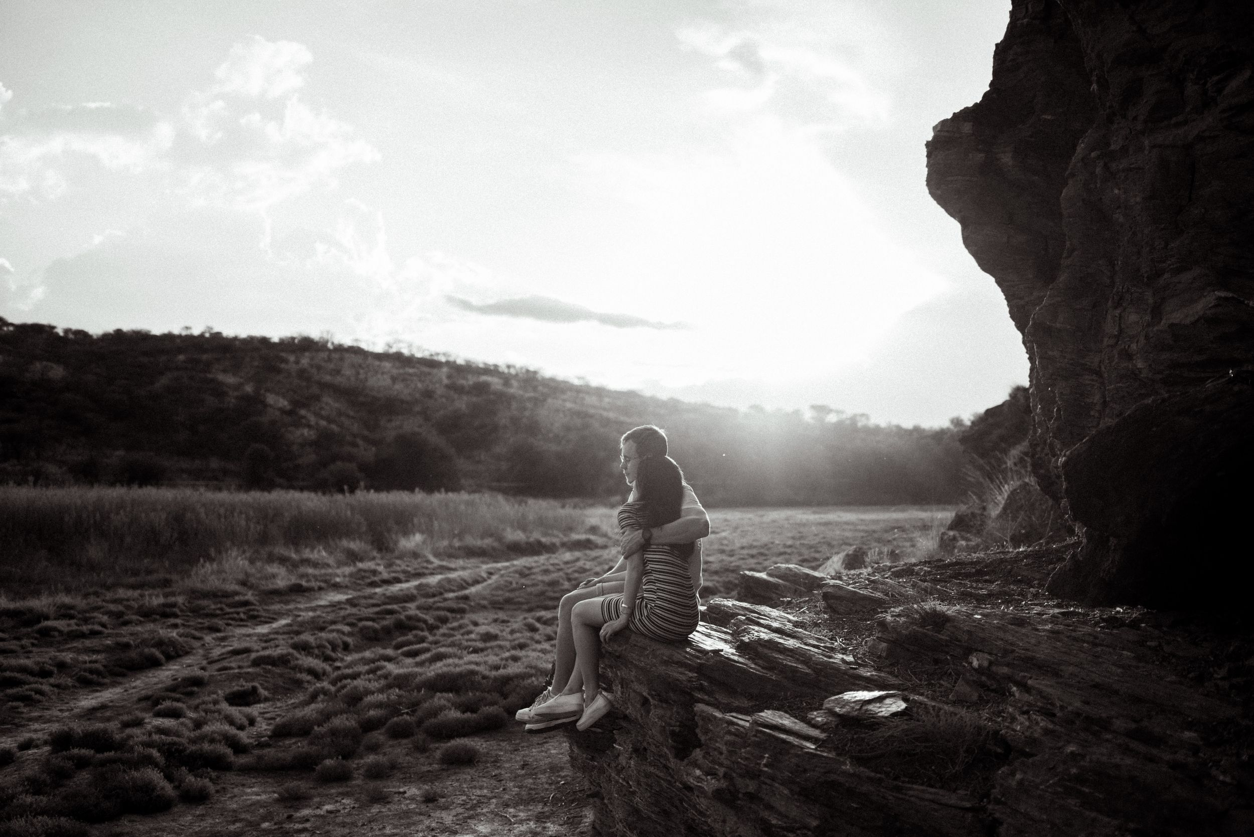 Silhouette of person sitting on rocky outcrop during sunset in black and white.