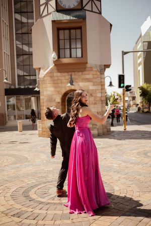 A woman in a flowing magenta gown twirls elegantly on a paved street corner with historic architecture.