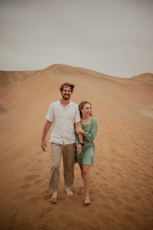 Barefoot couple walking together on desert sand dunes in casual attire.