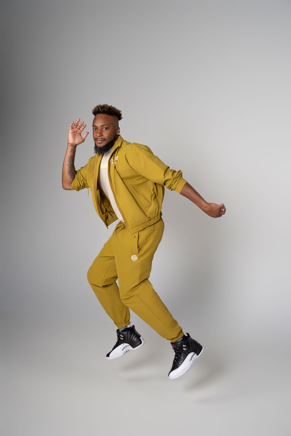 Energetic dancer in mustard yellow suit performs dynamic jumping poses against a gray studio backdrop.