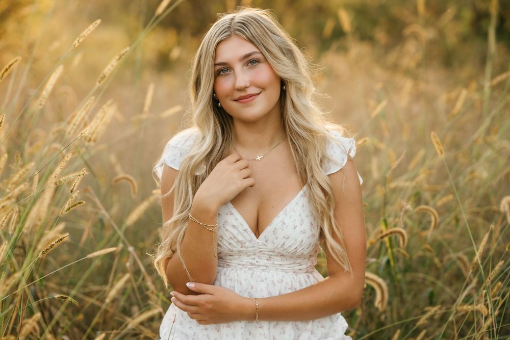 A person in a white lace dress poses in a golden wheat field during sunset.