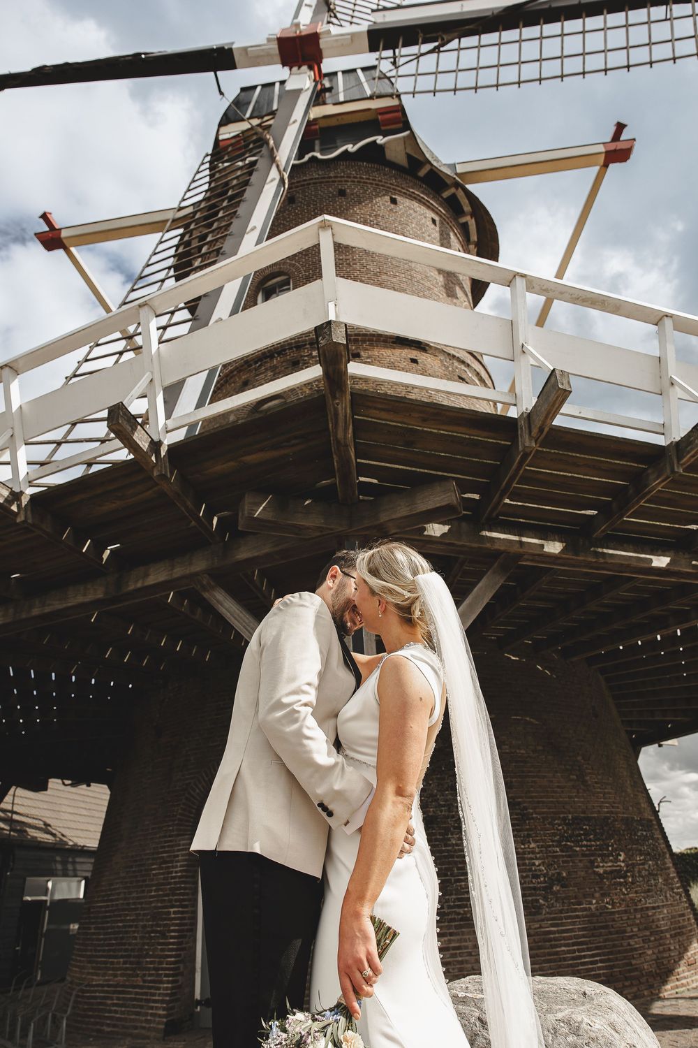 A series of romantic wedding photos showing a couple embracing near white pillars of a rustic outdoor venue.