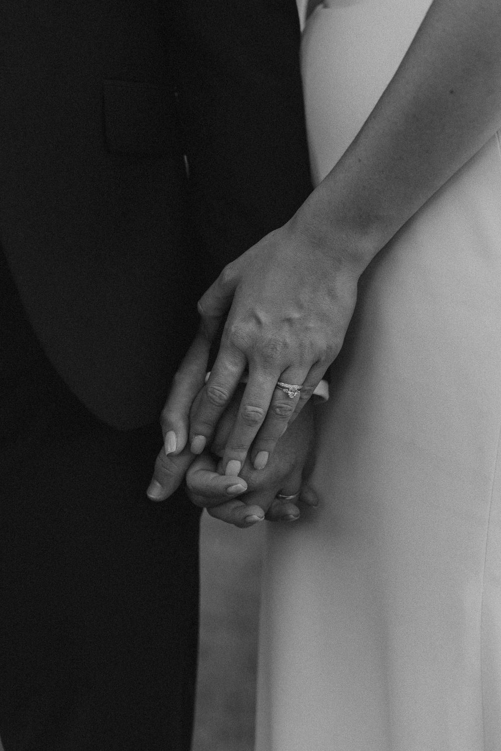 Black and white close-up of hands with wedding rings touching tenderly.