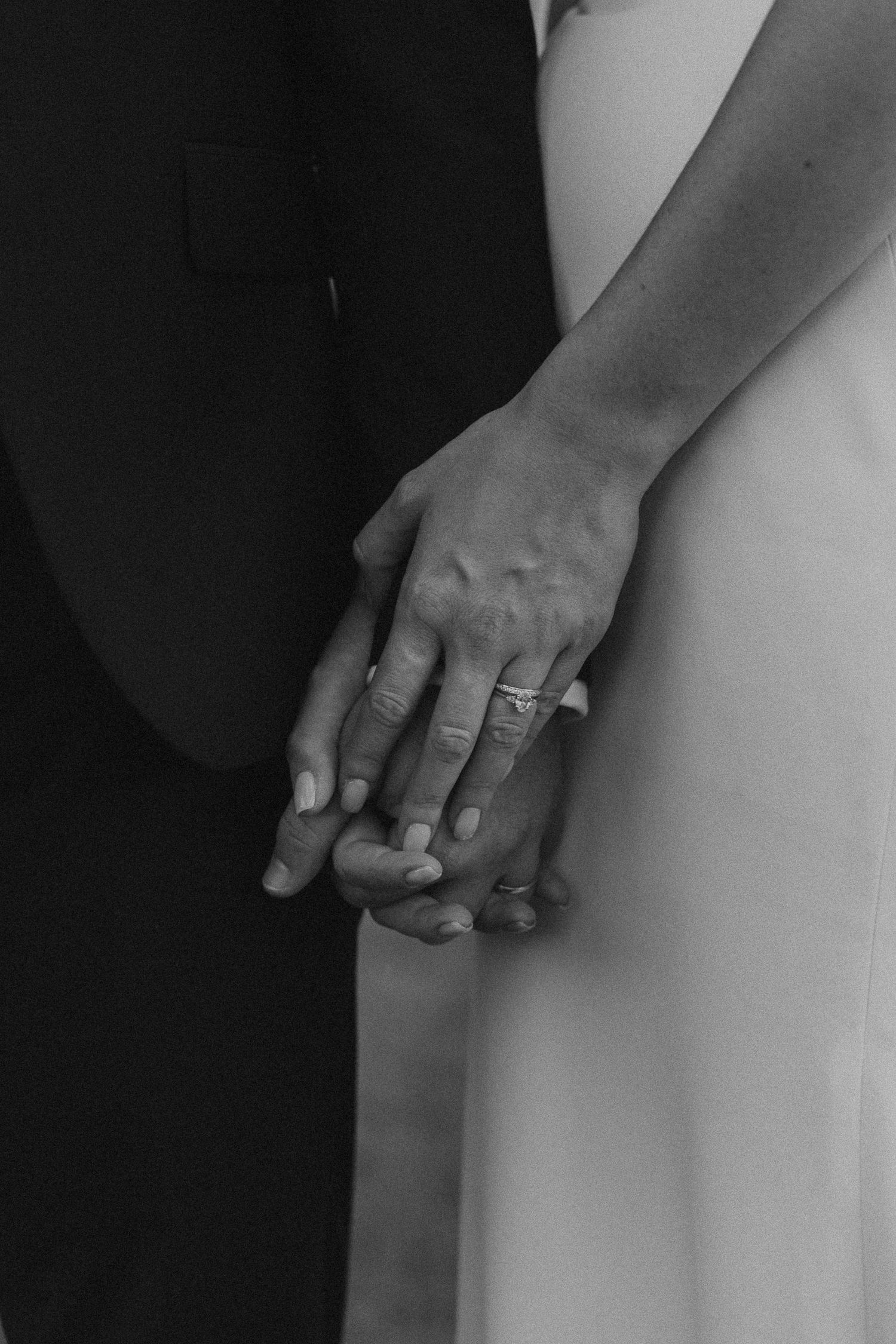 Black and white close-up of hands with wedding rings touching tenderly.