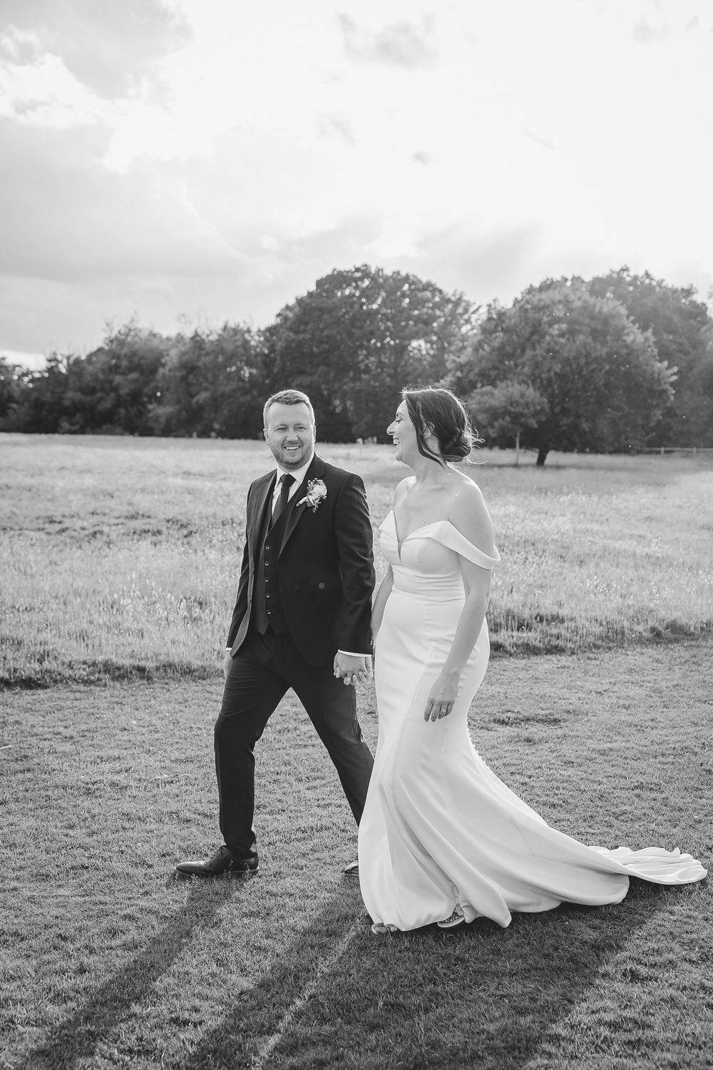 A couple in wedding attire sits together on a grassy hill in black and white photography.