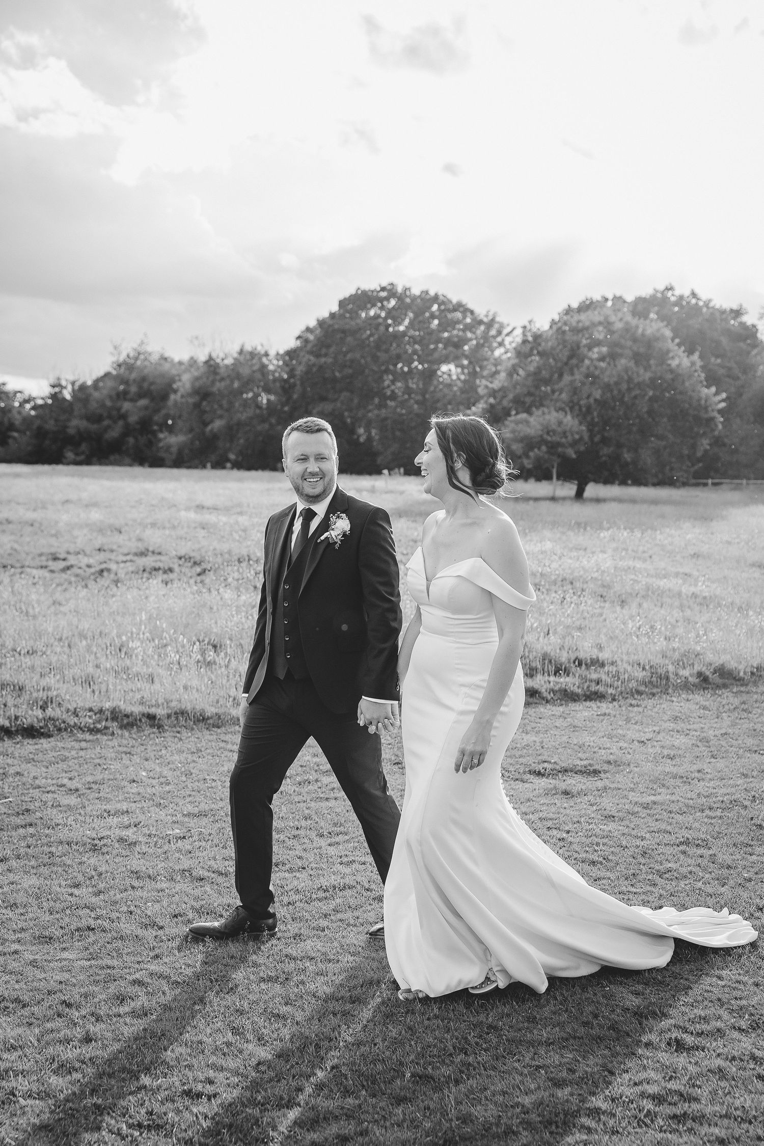A couple in wedding attire sits together on a grassy hill in black and white photography.