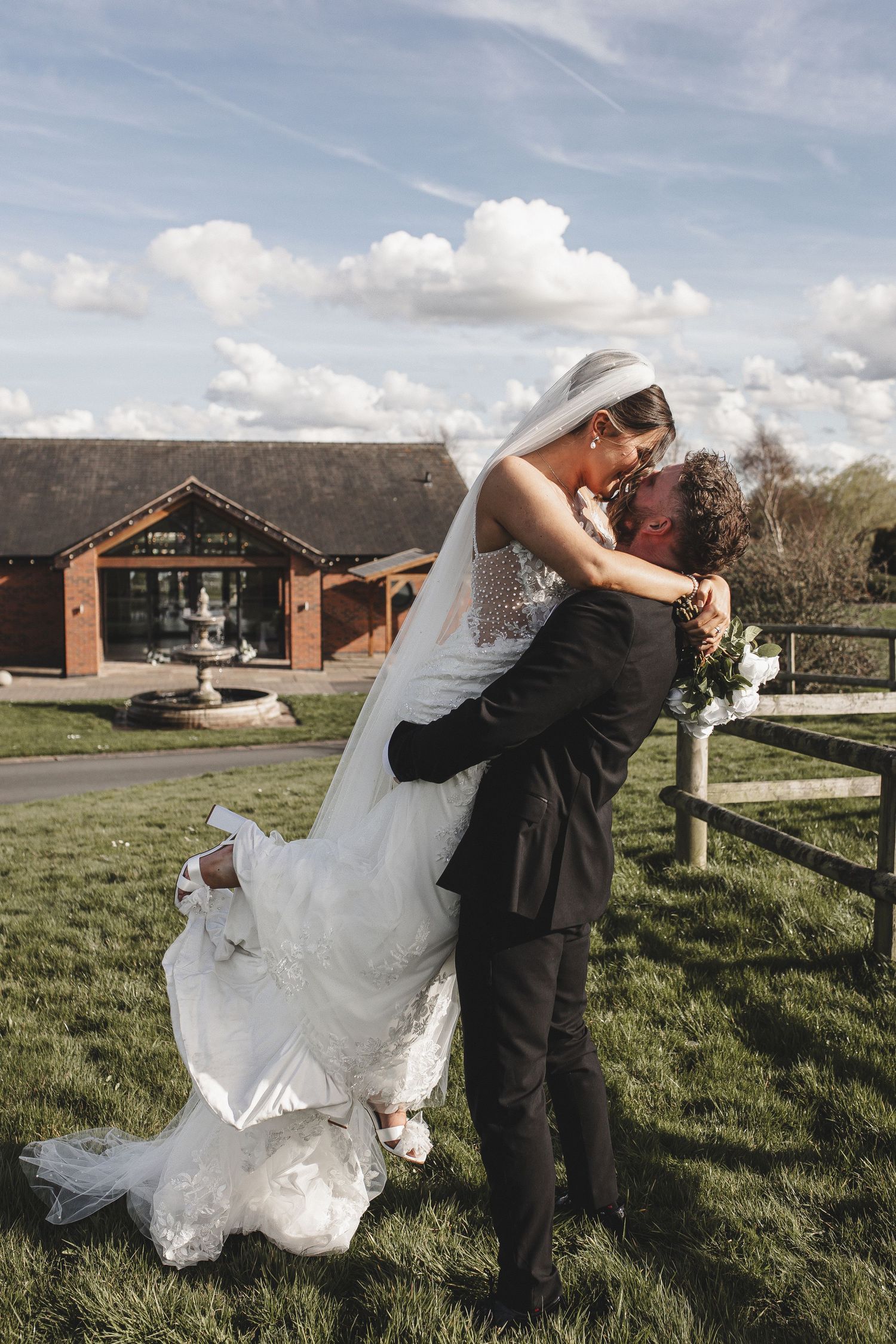 Romantic wedding couple dips and dances together in a grassy field on their special day.