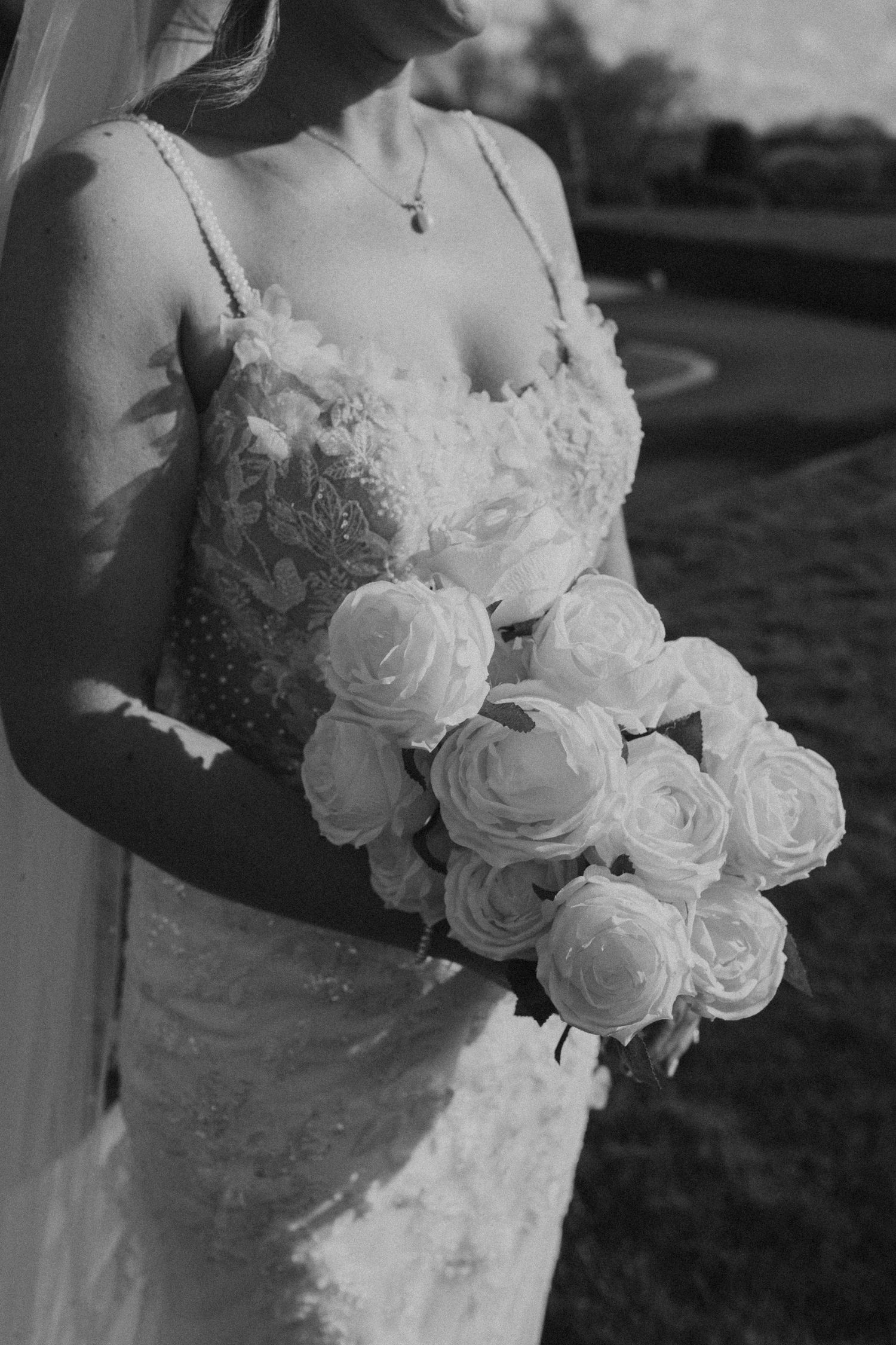 Black and white close-up of a bridal bouquet with white roses against a lace wedding dress bodice.