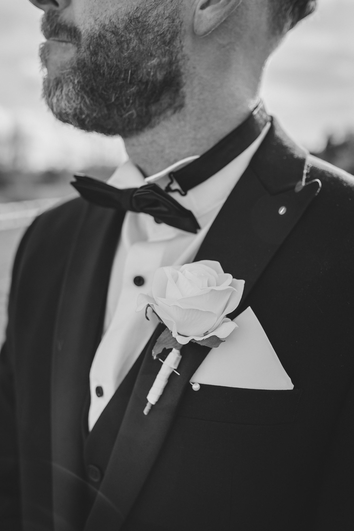 Close-up black and white photo of groomsmen in tuxedos with white boutonnieres at a formal wedding.