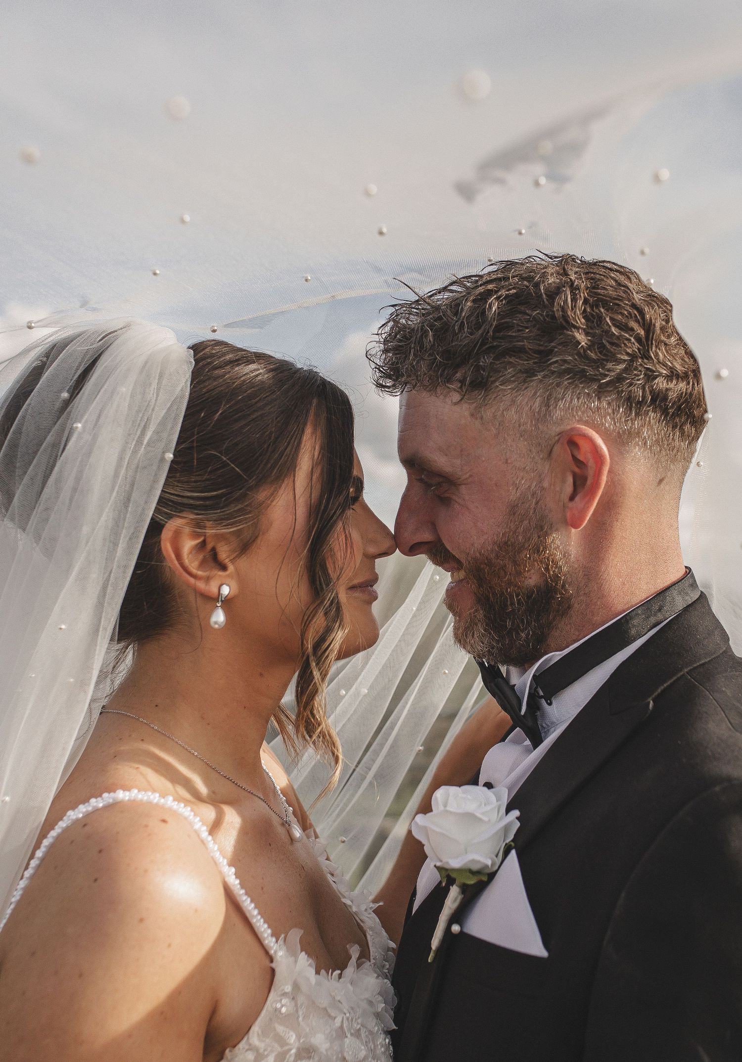 A tender moment between newlyweds as they share an intimate close-up under a flowing white veil.