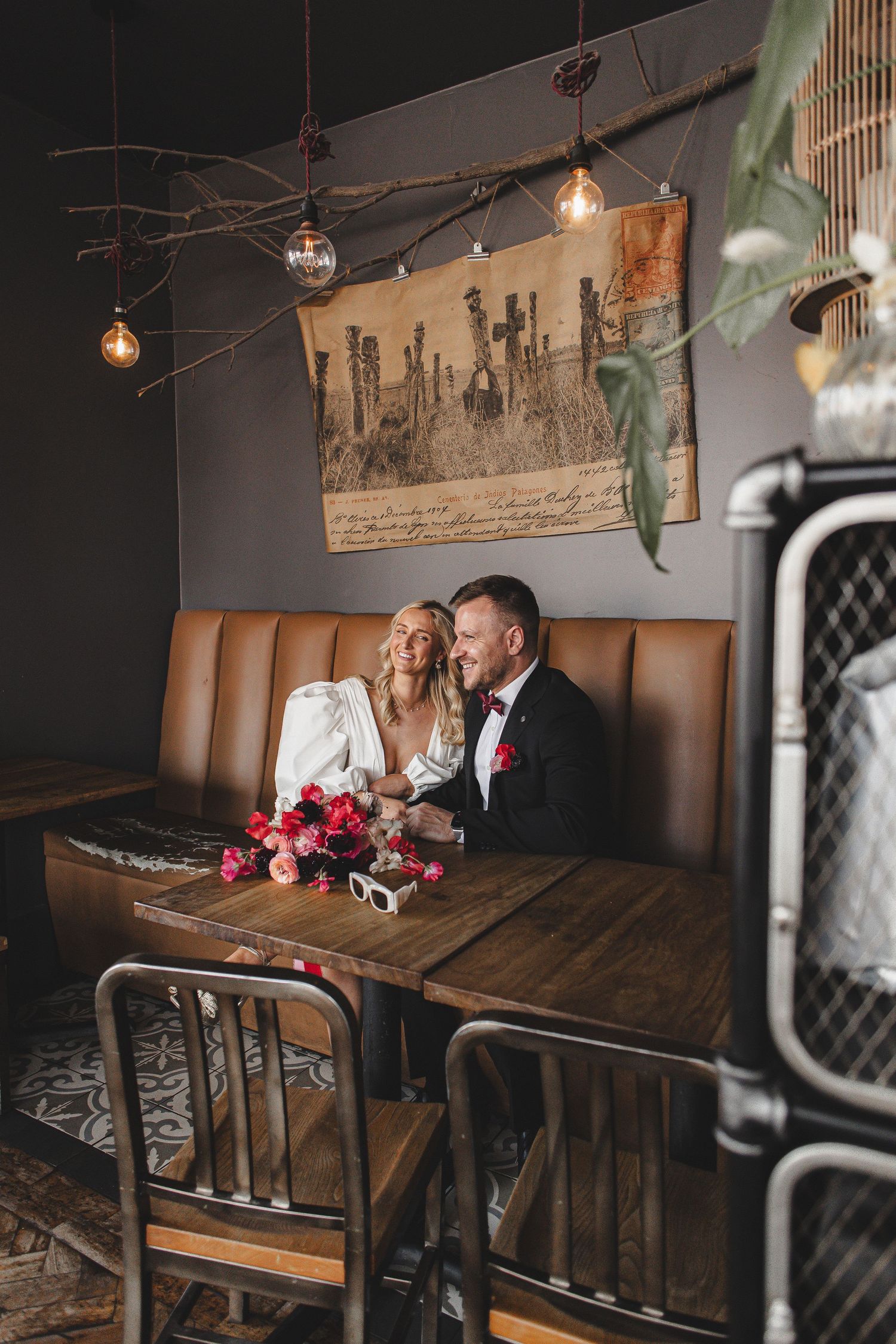 Couple shares intimate moment at rustic restaurant table with wooden decor and hanging pendant lights.
