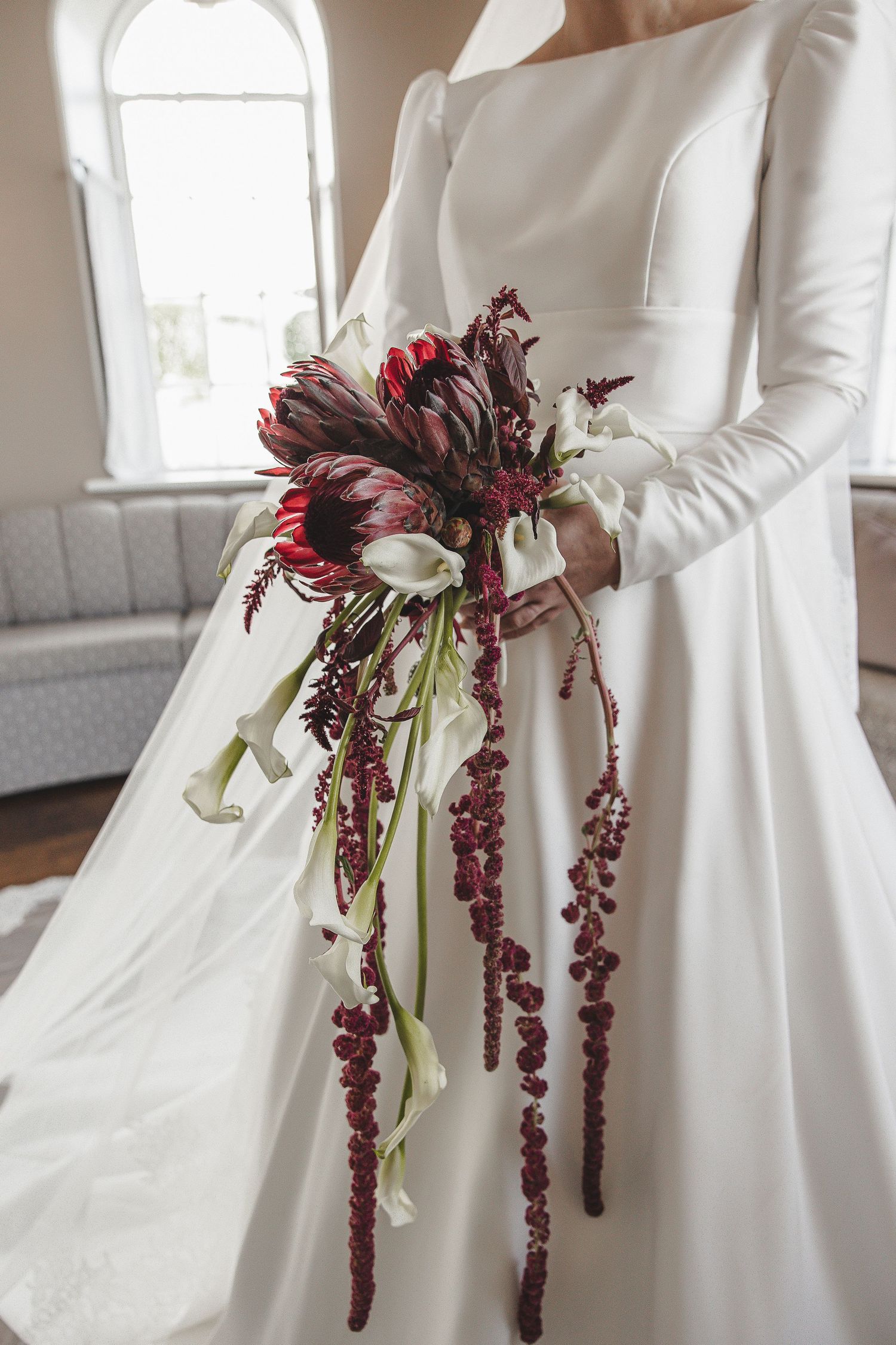 Three elegant white wedding dresses shown with burgundy floral bouquets featuring cascading amaranthus blooms.
