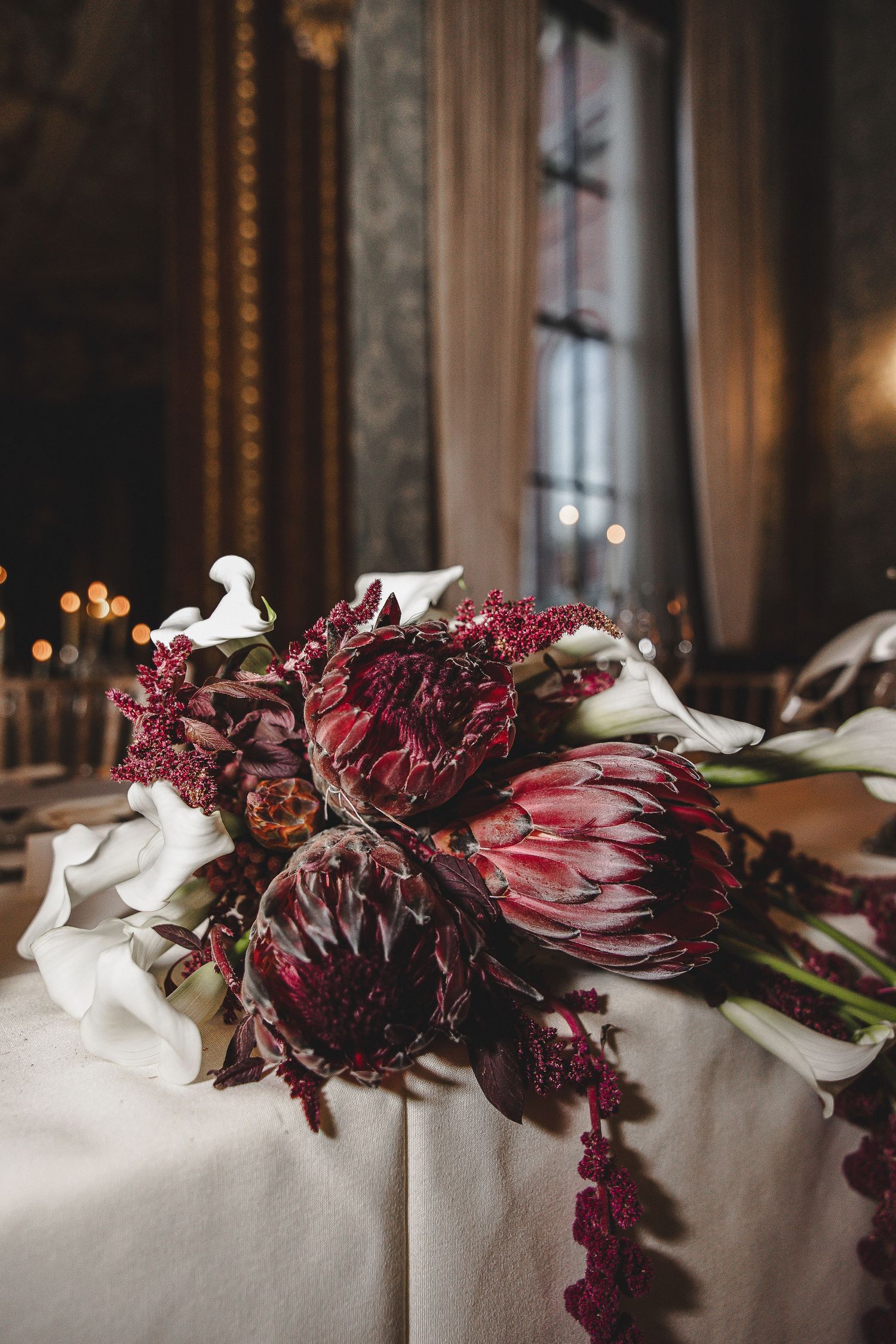 Dark burgundy dahlias and white flowers create an elegant floral arrangement against a soft backdrop.