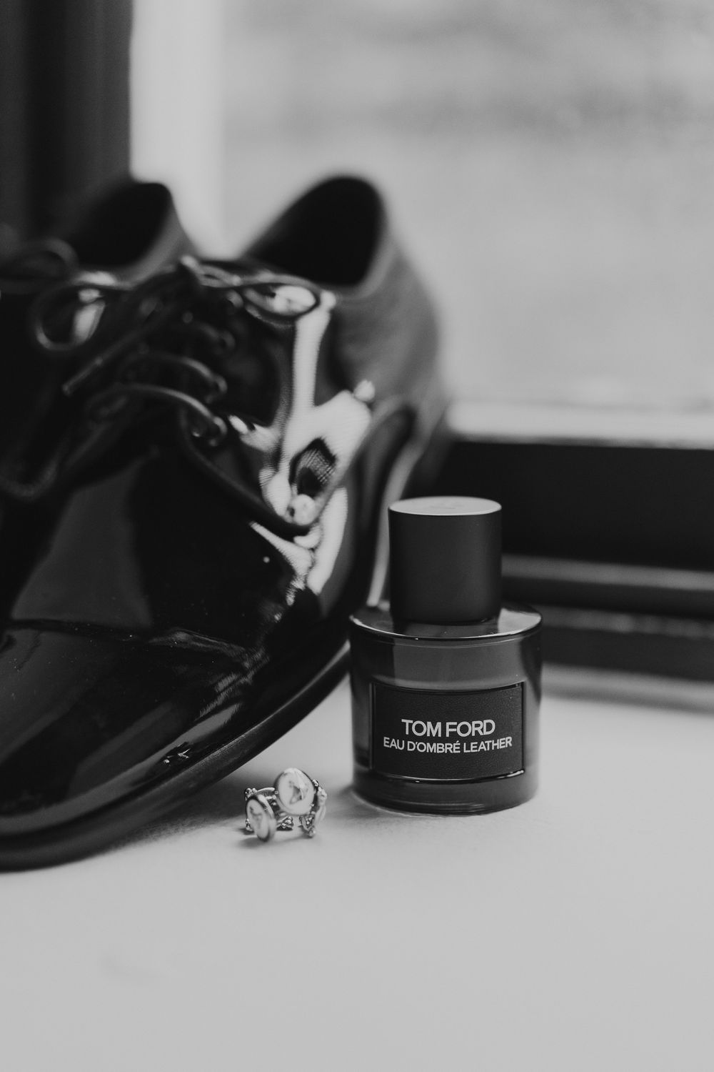 Black and white photo of elegant dress shoes and Tom Ford cologne on a minimalist surface.
