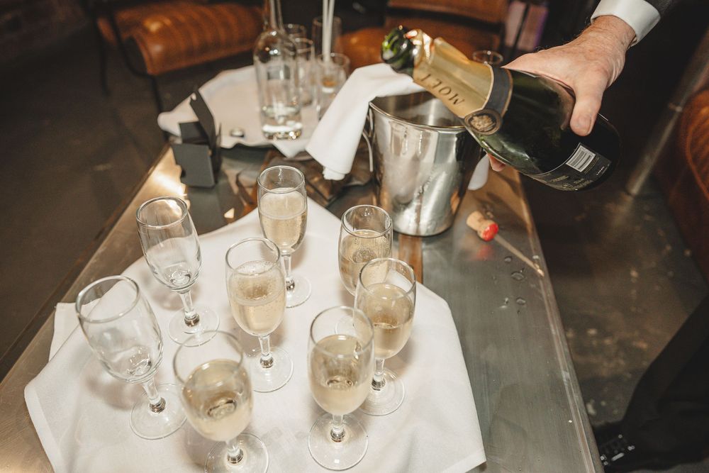 Several hands reach for wine glasses on a table during a celebratory toast at a social gathering.
